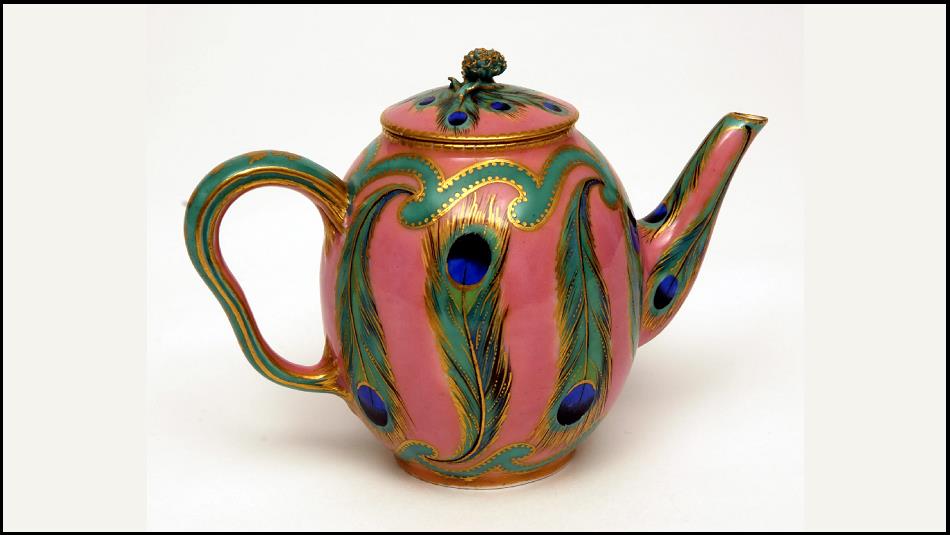 A colourful teapot with peacock feathers painted onto it.