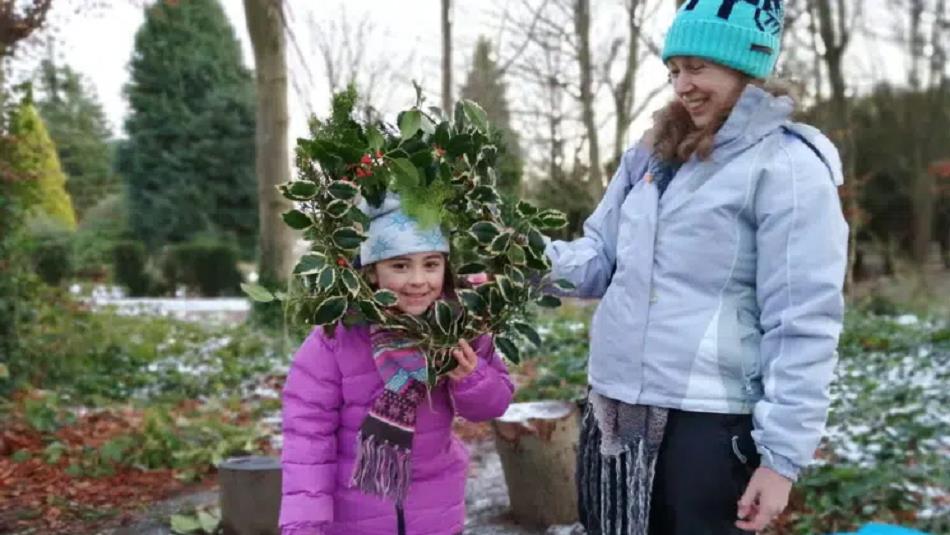 A child and an adult in the grounds of Ushaw peering through a handmade festive wreath.