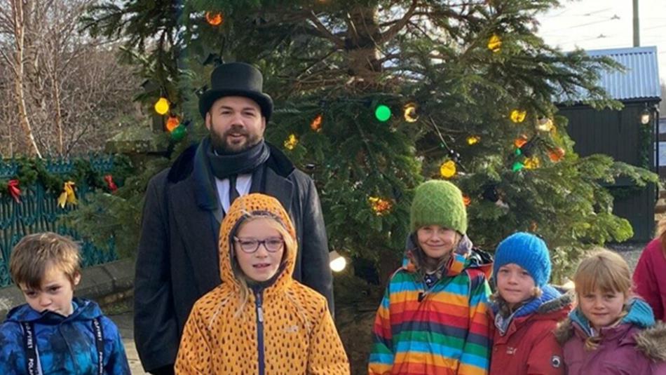 A staff member in a black top hat, posing for a photo with five children.