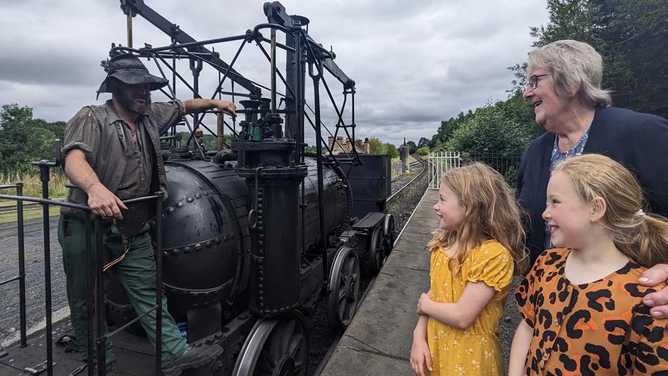 Two children and their grandmother speak to a Beamish member of staff in Georgian costume as he stands on a replica Georgian steam engine.