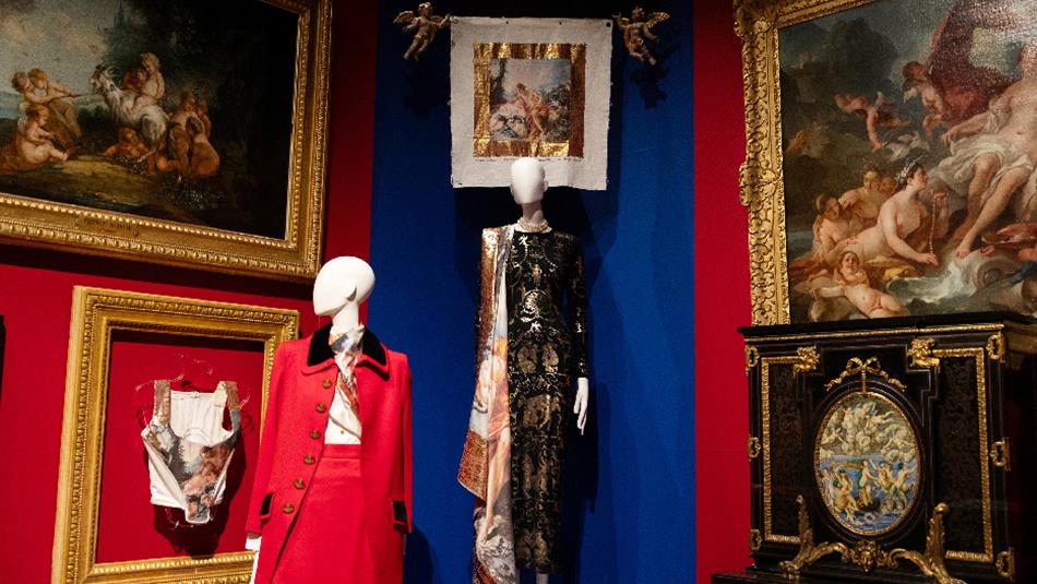 Photograph of a museum display featuring historical and artistic elements, including two mannequins dressed in elaborate costumes and framed classical