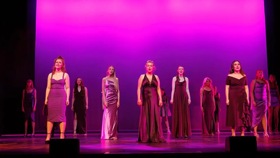 Performing Arts students of New College Durham's Class of 2025 on stage in long dresses.