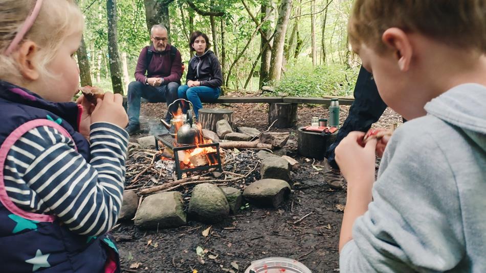 Children, accompanied by adults, enjoying bread on a stick by the campfire.