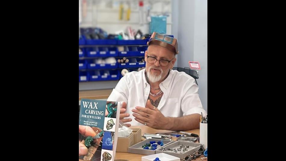 Russell Lownsbrough sitting at a table covered in wax materials giving a masterclass on wax carving.
