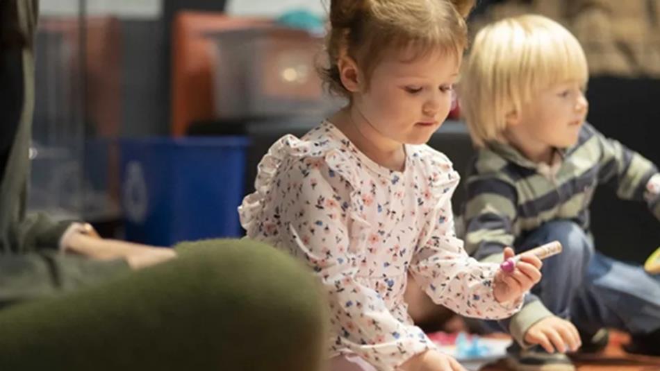 Child holding a crayon, sitting with other children at Little Dragons.