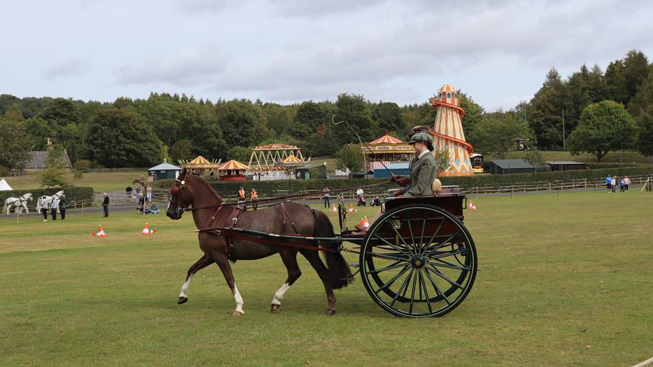 A horse, carriage and two drivers compete in the Attelage event in front of the Fairground at Beamish Museum.
