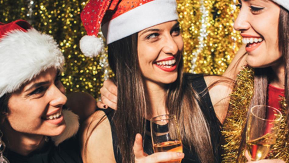 3 women in Santa hats laughing and drinking from champagne flutes.