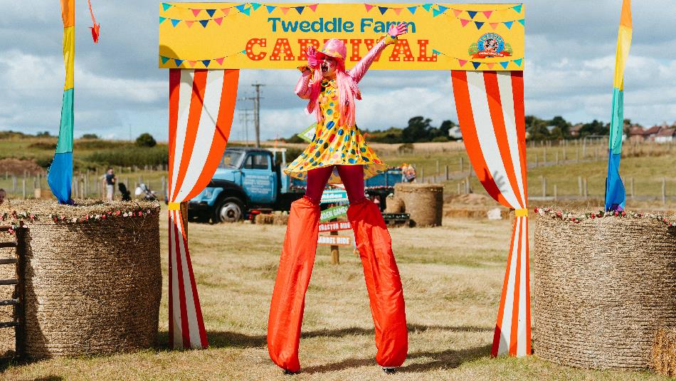 A performer singing on stilts between rolls of hay at Tweddle Carnival.