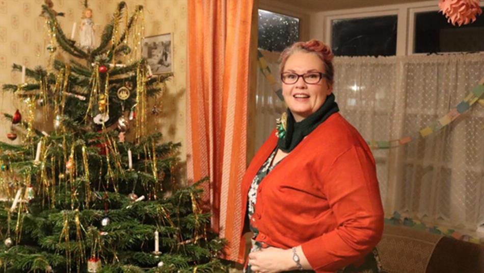A woman stands next to a Christmas tree with traditional decorations