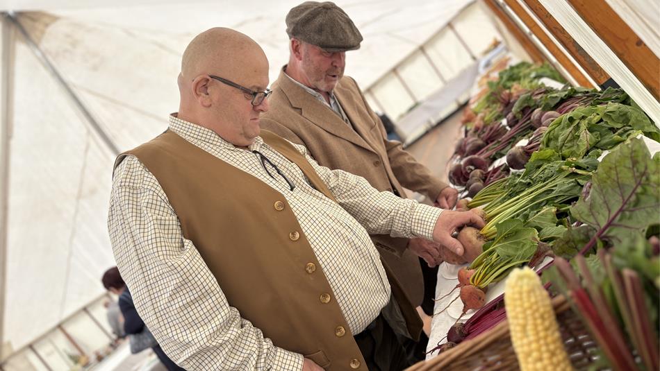 Two members of the Horticultural Show look at a display of vegetables.