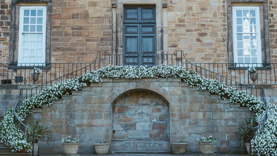 Lumley Castle exterior. Two staircases, bordered by shrubs, lead to a door.