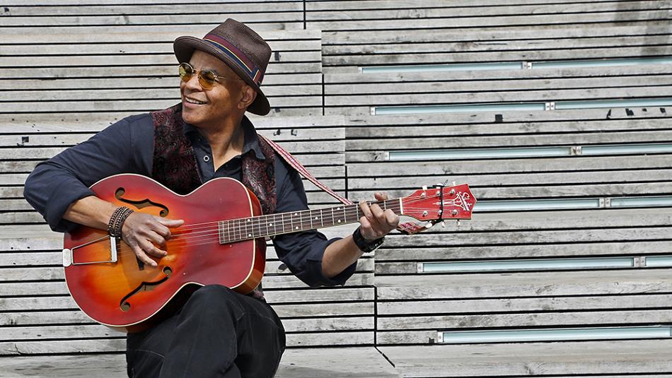 Guy Davis wearing a hat and holding a guitar