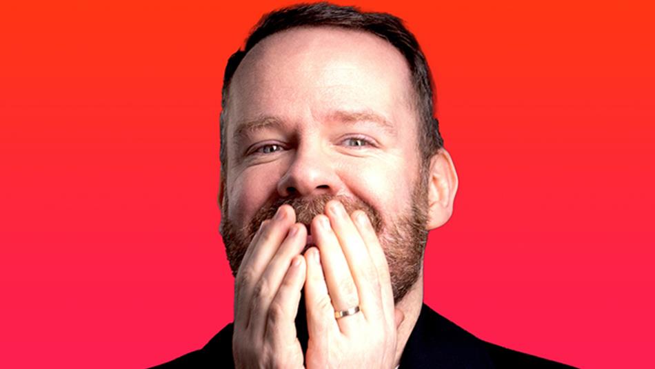 Headshot of Neil Delamere grinning with his hands covering his mouth.