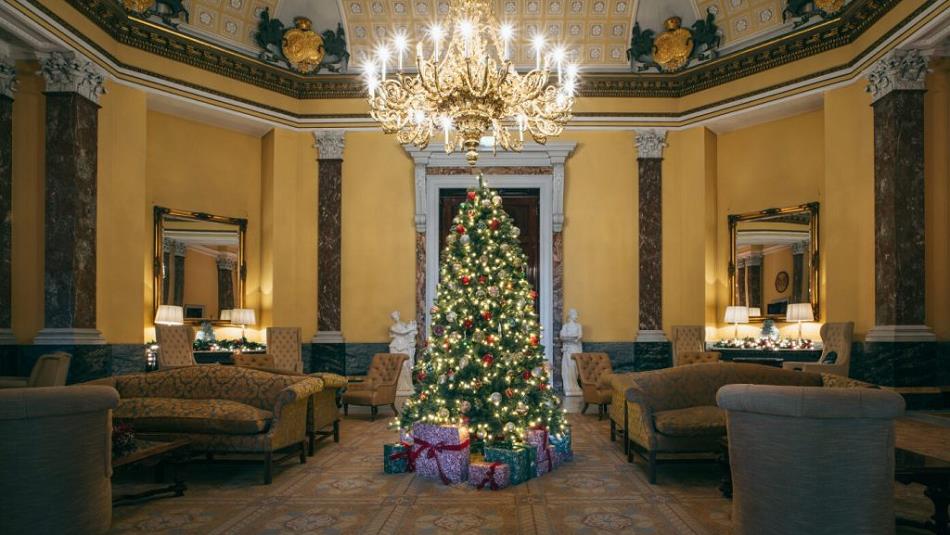 Christmas tree with presents under an opulent candelabra in a comfortable lounge area.