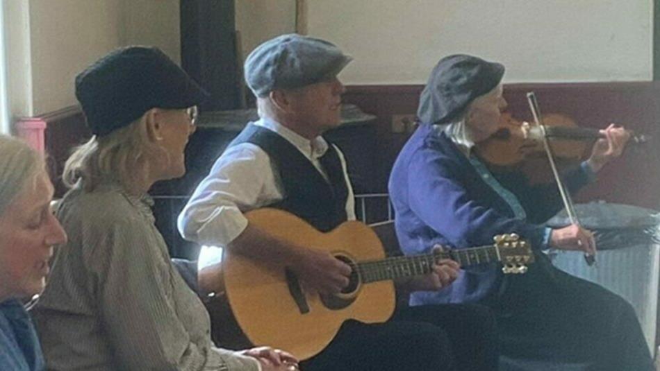 Folk musicians playing together in the Band Hall in The Pit Village.