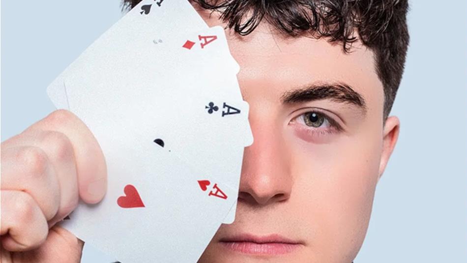 Close up of Tom Bolton holding a suit of aces which cover one side of his face.