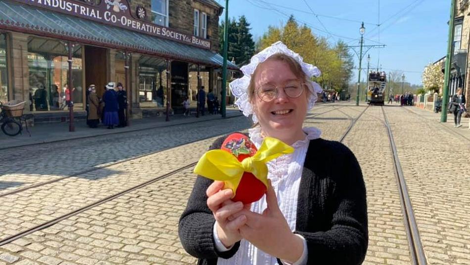 A member of staff in traditional clothing holding an Easter Egg with a yellow bow on it