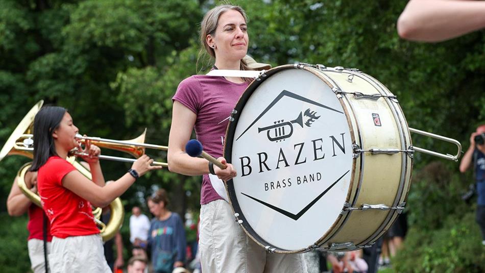 Woman playing a drum as part of, 'Brazen Brass Band'.