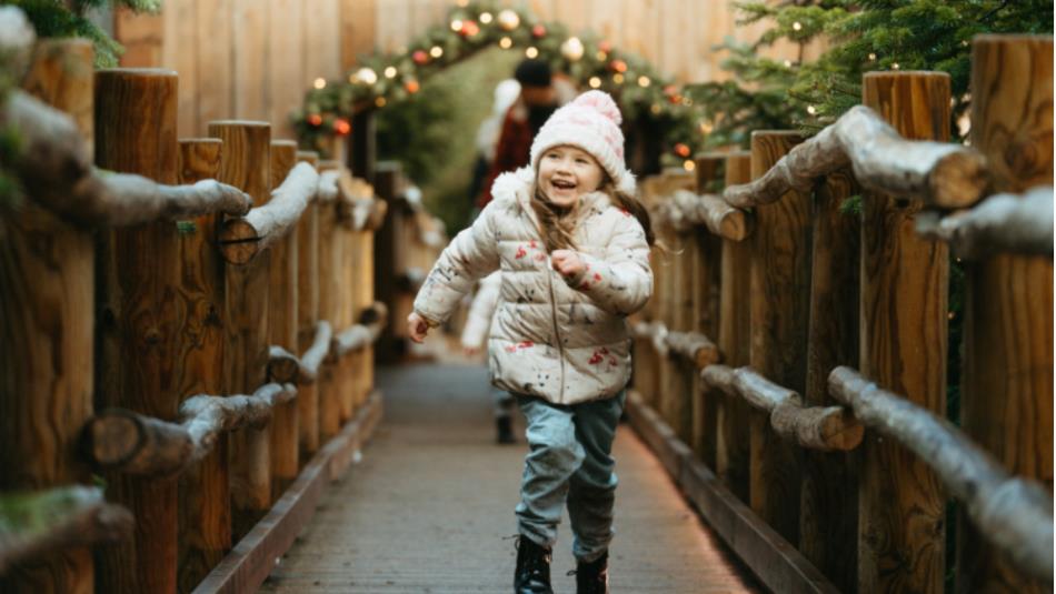 Small child, wearing winter clothes, running through a festive woodland trail