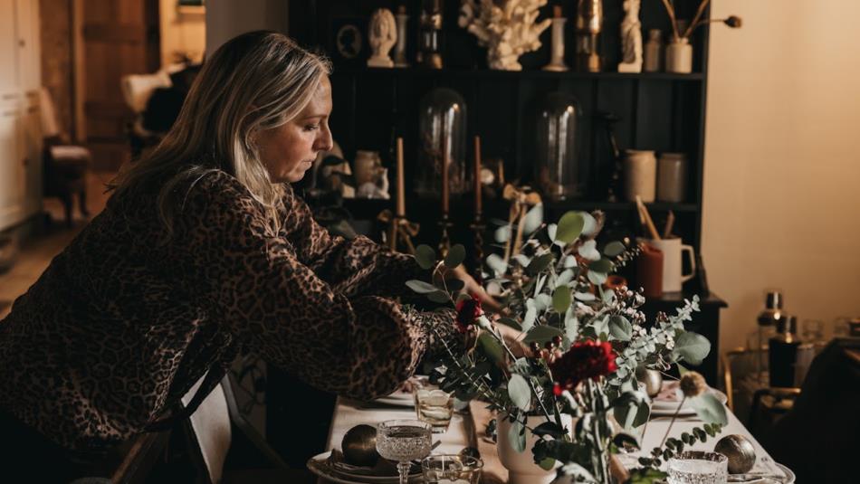A person tending to a festive dining room arrangement of festive flowers