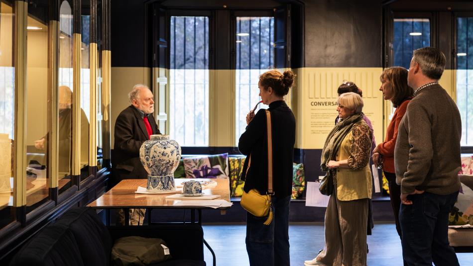 Photograph of a museum or gallery setting where a guide explains exhibits to a group of four visitors.