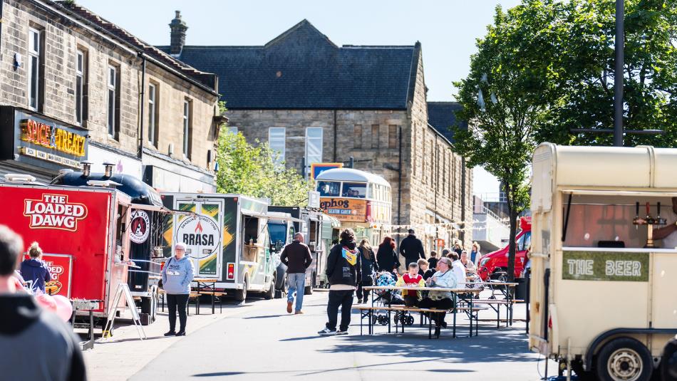A street full of food vendors and benches of people on a summers day