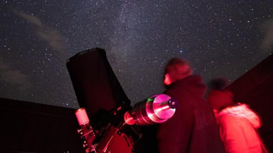 Two people looking up to a starry sky with a telescope