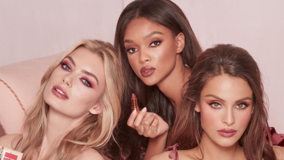 Three people holding Charlotte Tilbury makeup against a light pink background