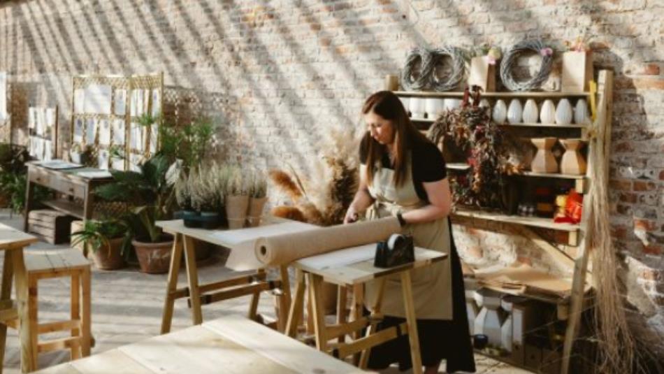 A person working in a sunny florist workshop, cutting paper over a wooden table