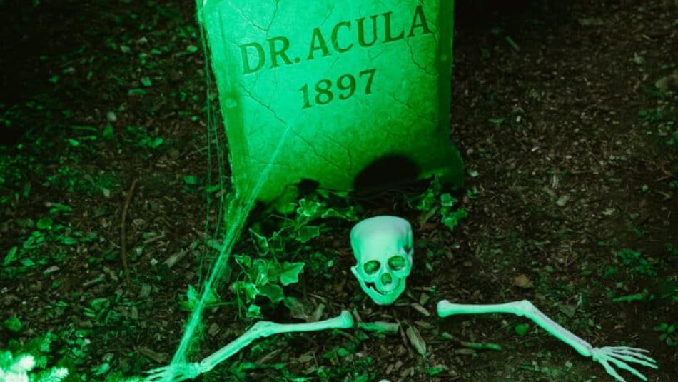 A spooky green grave in the forest saying "Dr.Acula 1897" with a skeleton coming out of the ground