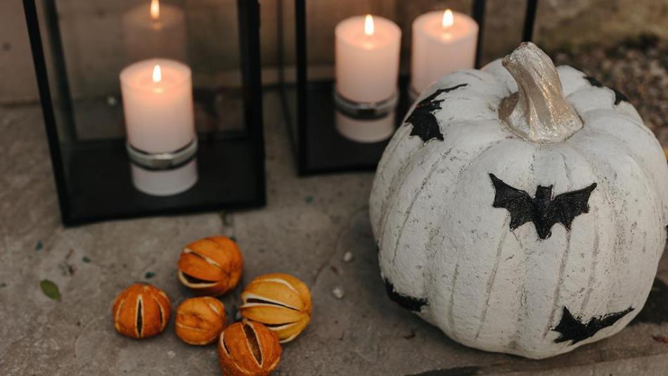 White painted pumpkins with bats, on a table surrounded by candles