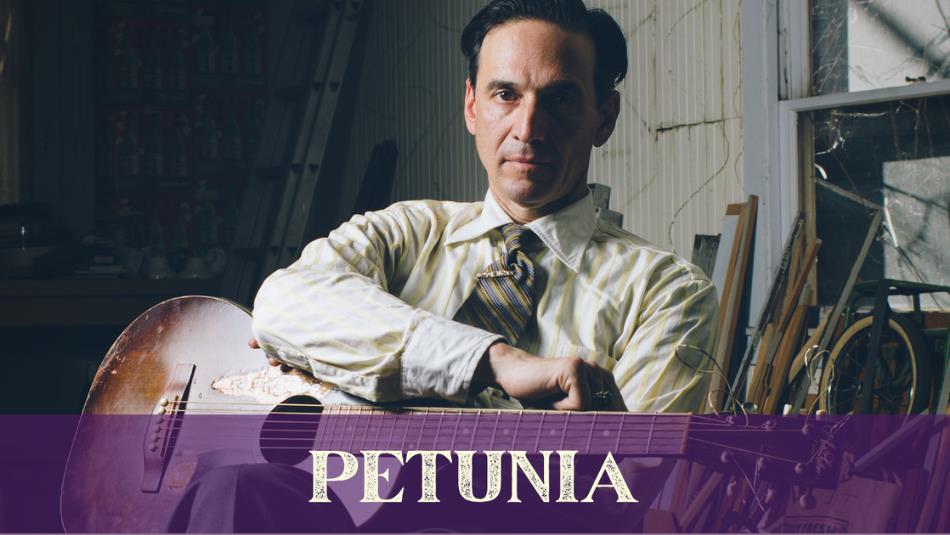 A person wearing a shirt and tie, holding a guitar. The text  underneath reads 'Petunia.'