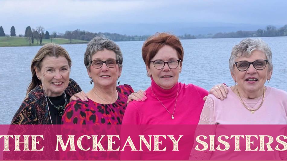 Four sisters, smiling shoulder to shoulder in pink clothing, in front of a body of water. The text 'The McKeaney Sisters' underneath.