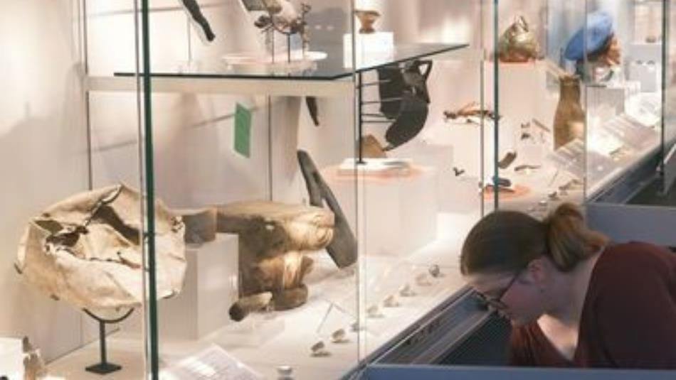 A museum exhibit with lots of old artefacts with a person tending to them in the right hand corner.