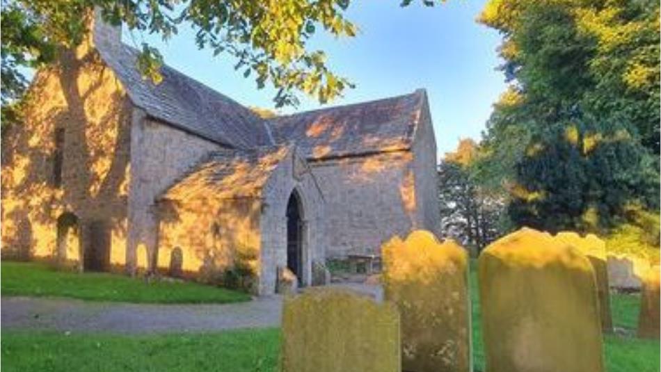 A church surrounded by trees and graves in the sunlight.