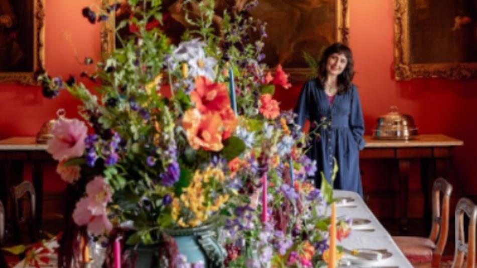 Person stood behind a large colour flower arrangement on a dining room table.