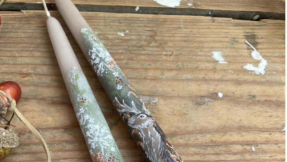 Two painted candle sticks with painted deer, on a wooden table.