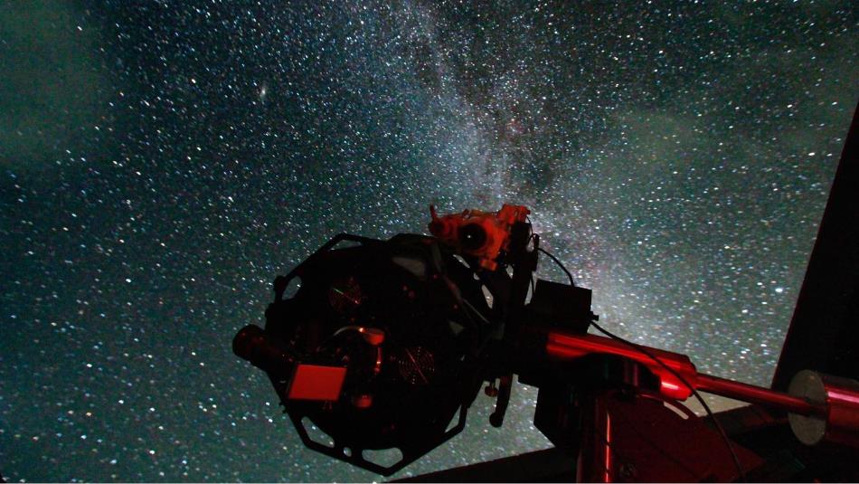 A telescope silhouetted against a star-filled night sky, with the Milky Way visible in the background.