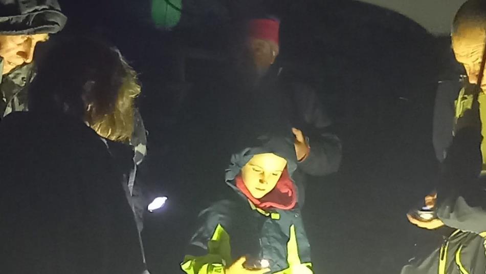 Participants in warm clothing gather around a moth trap during a nighttime wildlife survey, illuminated by a bright light.