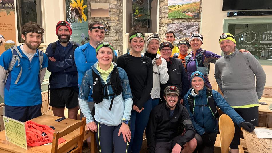 Group of runners wearing head torches pose together indoors after a night time run.