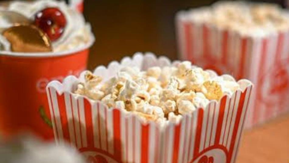 A close up of a tub of popcorn and a drink.