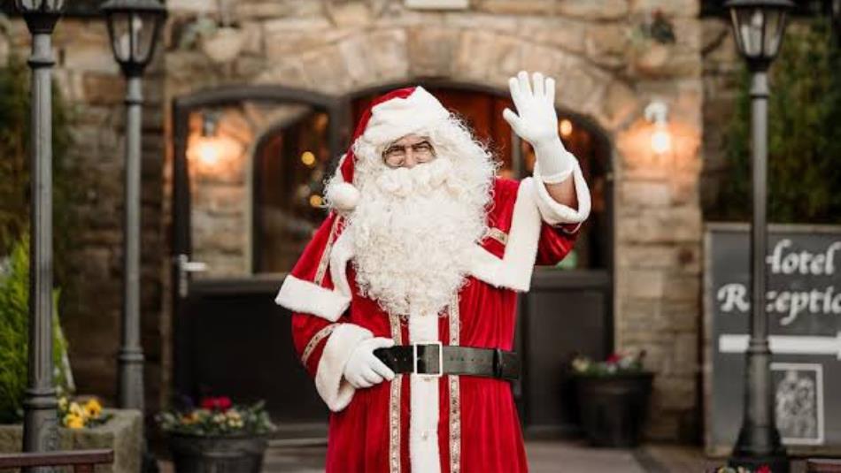 Santa standing in front of a stone building waving