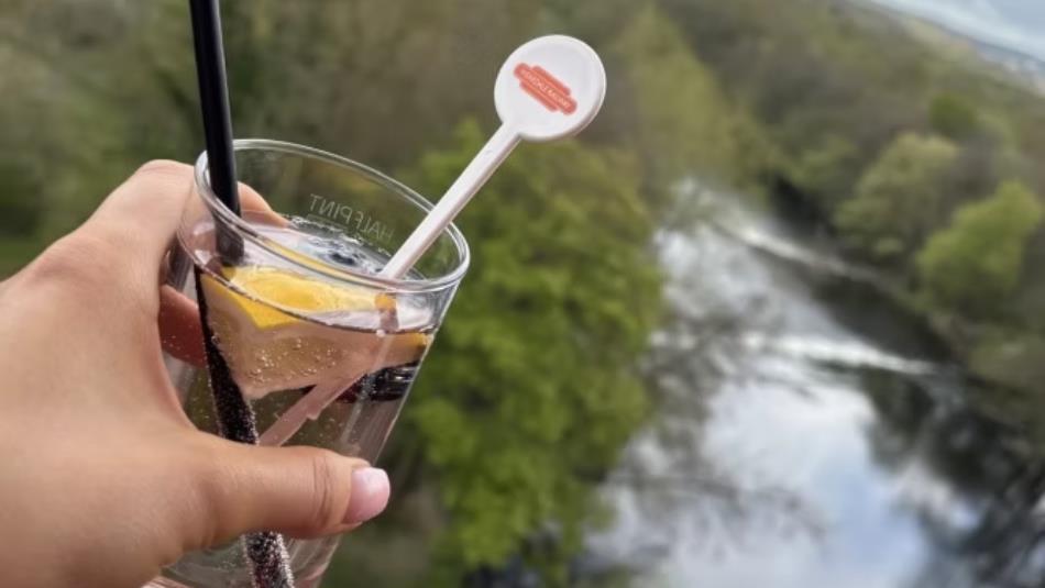 A hand holding a drink over a river with the Weardale Railway logo.