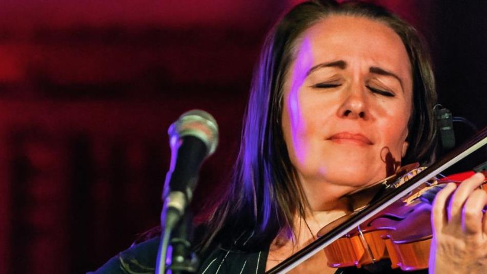 A close up image of a person playing the violin with their eyes closed on a stage.