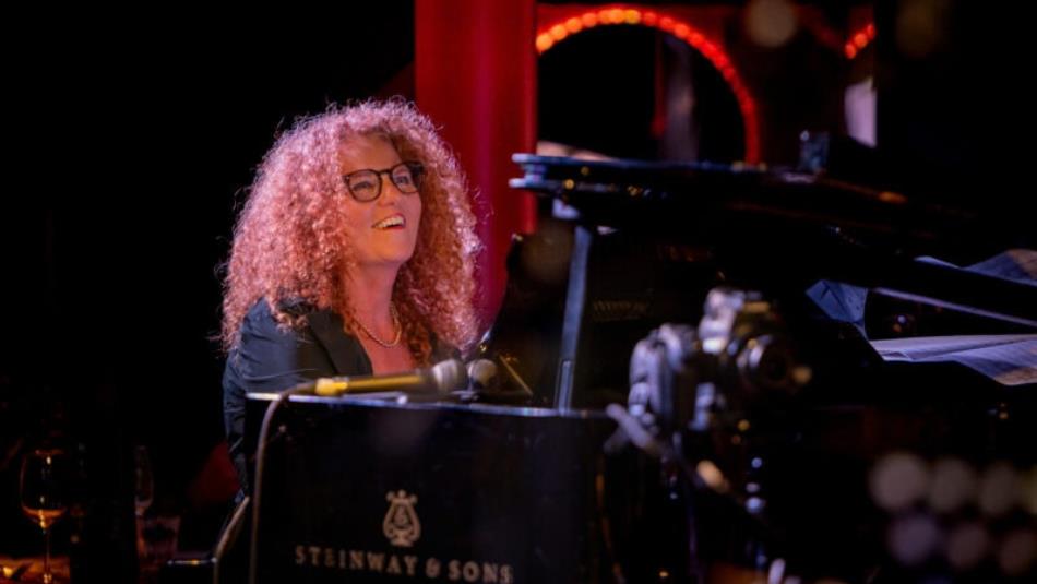 Person smiling whilst playing the piano on stage.