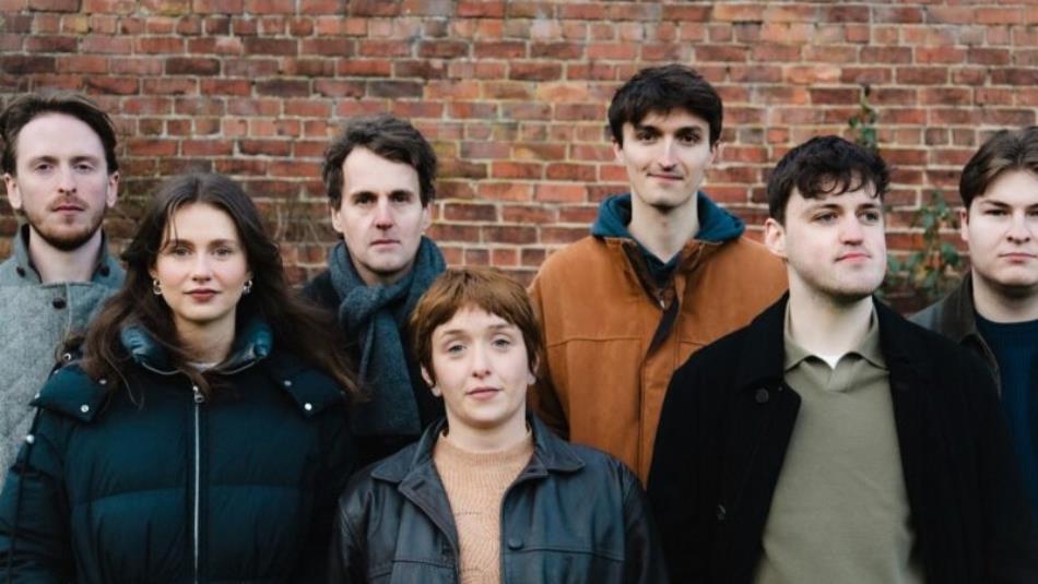 Seven people stood against a brick wall.