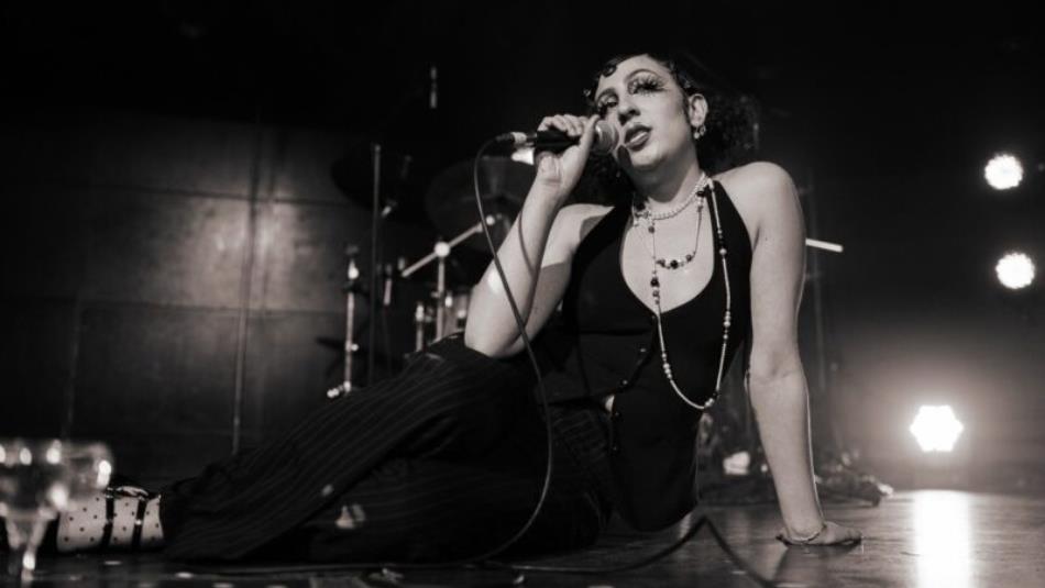 A person sat on stage singing into a microphone, the image is in black and white.