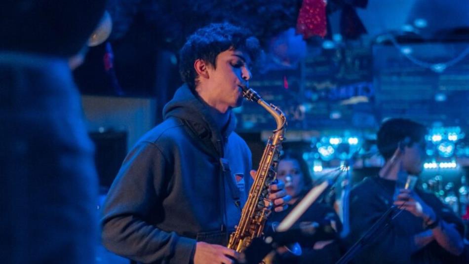 A person playing the saxophone, with a blue background.
