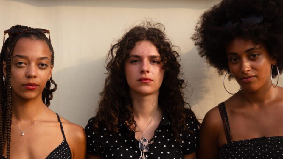 Three people standing against a wall, looking straight ahead at the camera.