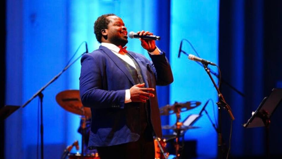 A person singing into a microphone on a blue stage.